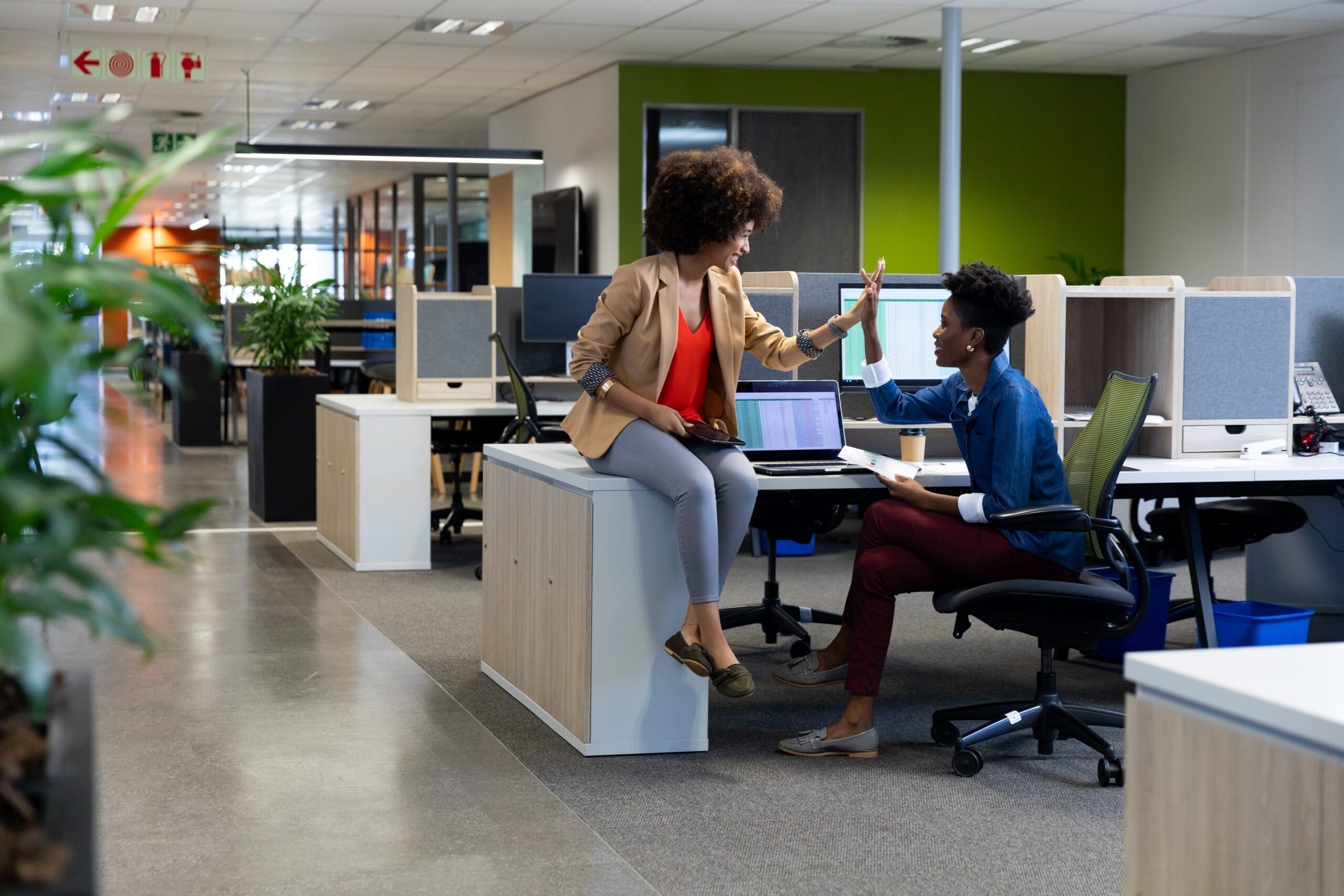 happy biracial businesswomen giving high five meeting while sitting cubicle workplace scaled